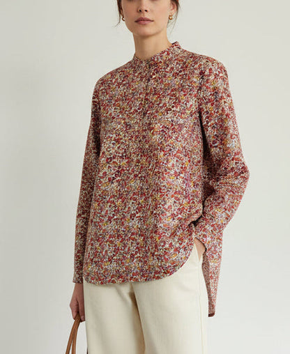 A long-sleeve button-up shirt with a dense red, pink, and yellow floral print, hanging on a wooden hanger against a plain off-white wall.